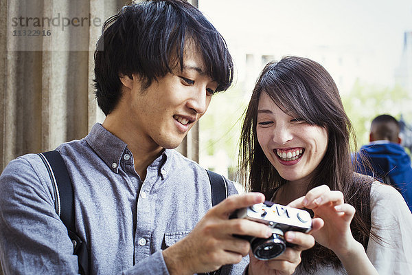 Ein junger Japaner und eine junge Japanerin genießen einen Tag in London  halten eine Digitalkamera in der Hand und lächeln.