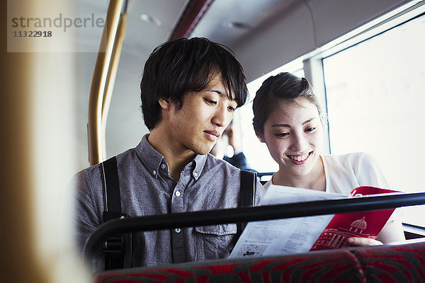 Ein junger Japaner und eine junge Japanerin genießen einen Tag in London und fahren in einem Doppeldeckerbus.