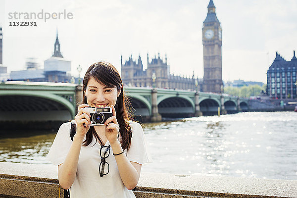 Eine junge Japanerin genießt einen Tag in London und steht auf dem Queen's Walk an der Themse.