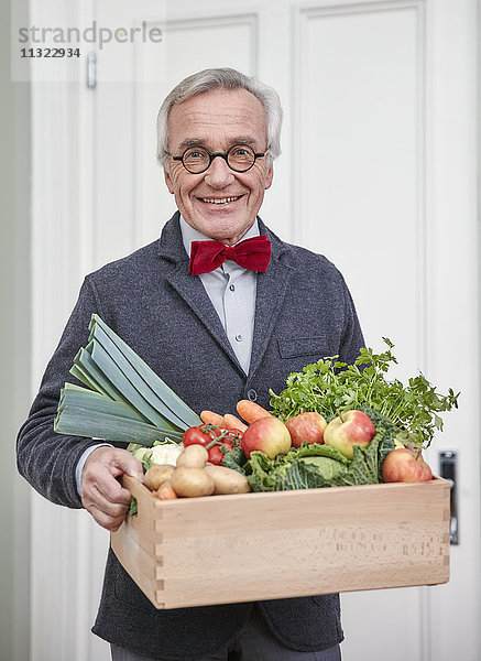Porträt eines lächelnden älteren Mannes  der eine Schachtel mit Produkten hält.