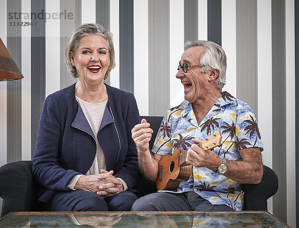 Glückliches Seniorenpaar mit Mann in hawaiianischem Hemd beim Ukulelele spielen