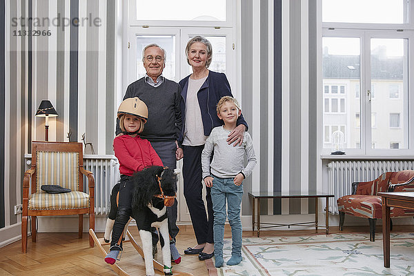 Großeltern und Enkelkinder mit Schaukelpferd im Wohnzimmer