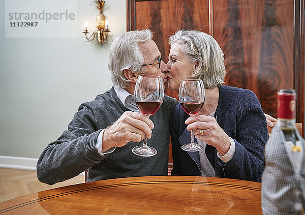 Seniorenpaar mit Rotweingläsern beim Küssen