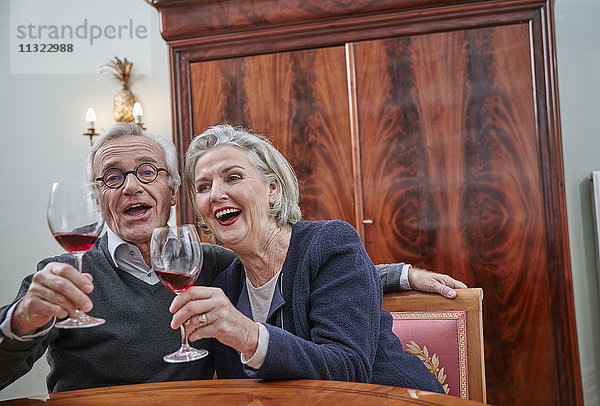 Fröhliches Seniorenpaar singt und trinkt Rotwein
