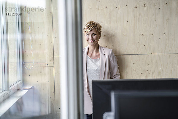 Lächelnde Geschäftsfrau an der Holzwand im Büro