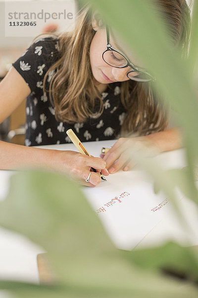 Ein junges Mädchen mit Brille  das an einem Tisch arbeitet  einen Stift benutzt  schreibt und zeichnet.