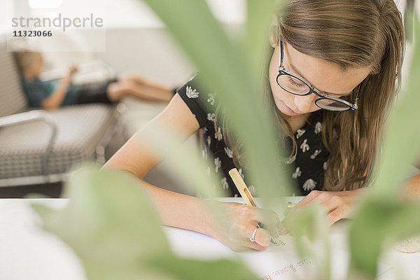 Ein junges Mädchen mit Brille  das an einem Tisch arbeitet  einen Stift benutzt  schreibt und zeichnet.