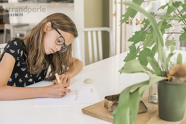 Ein junges Mädchen mit Brille  das an einem Tisch arbeitet  einen Stift benutzt  schreibt und zeichnet.