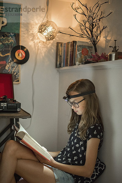 Ein Mädchen  das in einer ruhigen Ecke mit einer Stirnlampe ein Buch liest.