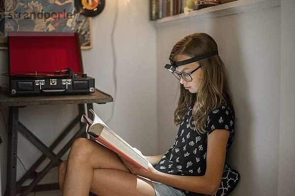 Ein Mädchen  das in einer ruhigen Ecke mit einer Stirnlampe ein Buch liest.