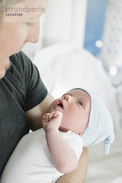 Ein Vater hält ein kleines Baby in der Hand  das Baby öffnet seinen Mund in einer Spiegelaktion dem Vater  der seinen öffnet.