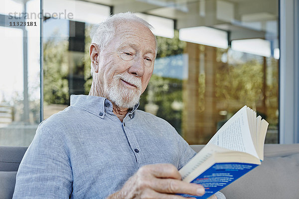 Älterer Mann auf der Terrasse sitzend Lesebuch