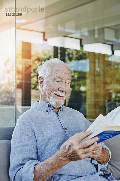 Älterer Mann auf der Terrasse sitzend Lesebuch