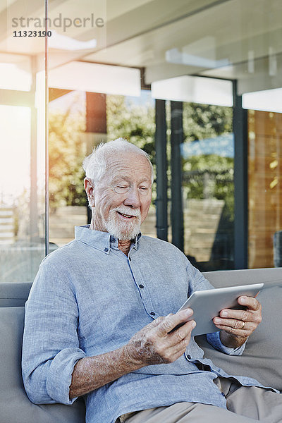 Senior Mann sitzt auf der Terrasse und liest ebook