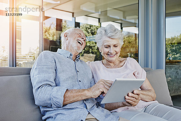 Seniorenpaar auf der Terrasse sitzend mit digitalem Tablett