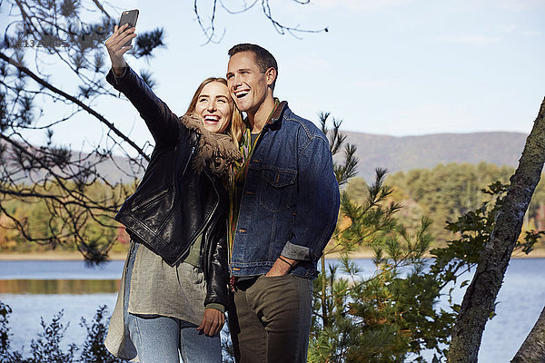 Zwei Menschen  Mann und Frau  die im Herbst am Ufer eines Sees ein Selfie machen.