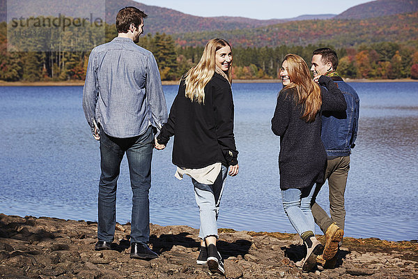 Vier Menschen gehen  Paare Hand in Hand  am Ufer eines Sees entlang.