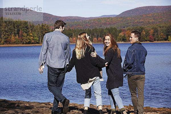 Vier Menschen gehen  Paare Hand in Hand  am Ufer eines Sees entlang.