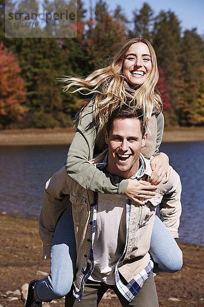 Ein Mann schenkt einer jungen Frau im Herbst ein Huckepack an einem See