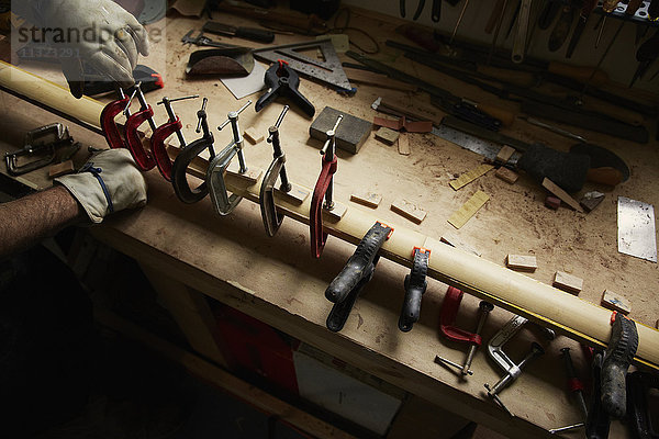 Ein Zimmermann  der Schutzhandschuhe trägt und Klammern an einem Stück Holz verwendet.