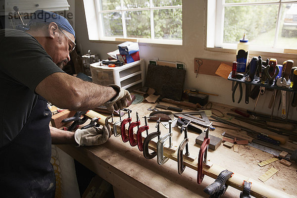 Ein Bogenbauer  der in seiner Werkstatt an einem Holzbogen arbeitet und das Holz durch Festhalten in Klammern formt.