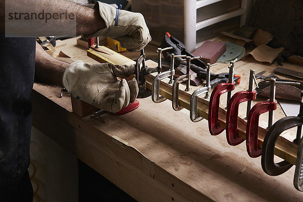 Ein Bogenbauer  der in seiner Werkstatt an einem Holzbogen arbeitet und Klammern auf dem Holz anbringt.