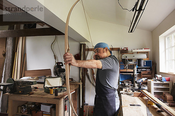 Ein Mann testet einen handgefertigten Bogen  indem er an der Bogensehne zieht.