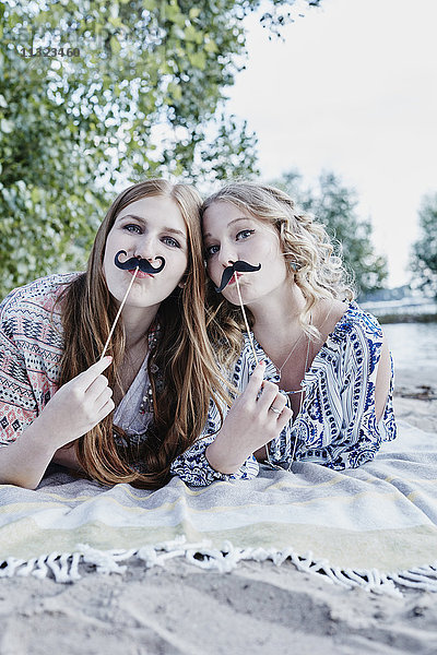 Porträt von zwei Teenagern mit Schnurrbart auf Decke am Strand liegend