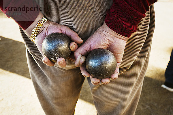 Ein Mann hält hinter seinem Rücken zwei Boule  kleine Metallkugeln in der Hand.