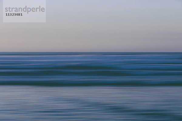 Meereswellen und der Blick vom Strand in der Abenddämmerung auf den Horizont über dem Meer.