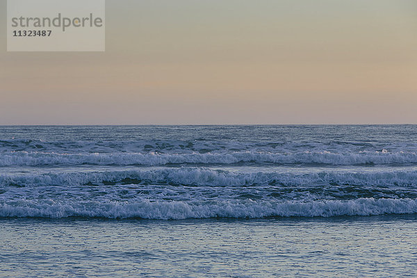 Meereswellen und der Blick vom Strand in der Abenddämmerung auf den Horizont über dem Meer.