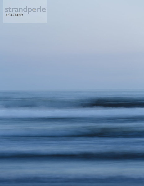 Meereswellen und der Blick vom Strand in der Abenddämmerung auf den Horizont über dem Meer.