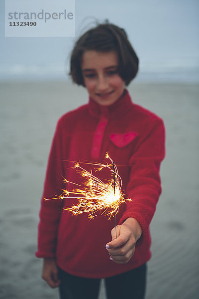 Ein junges Mädchen hält in der Abenddämmerung am Strand eine brennende Wunderkerze in der Hand.