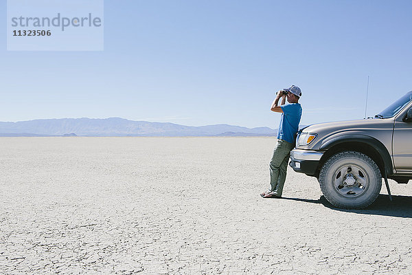 Mann steht auf riesiger Wüste  schaut durch ein Fernglas und lehnt sich an einen Lastwagen  Black Rock Desert