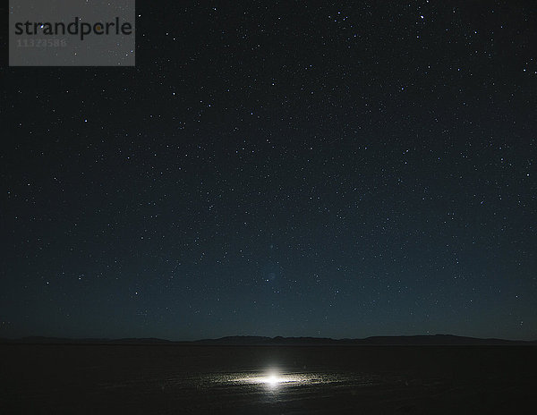Glühendes helles Licht auf Playa  Nachthimmel und Milchstraße darüber  Schwarze Steinwüste  Nevada