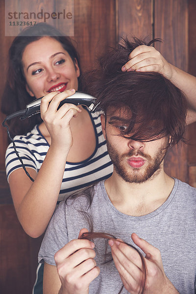 Junger Mann bekommt einen Haarschnitt von seiner Freundin mit einer Haarschneidemaschine.