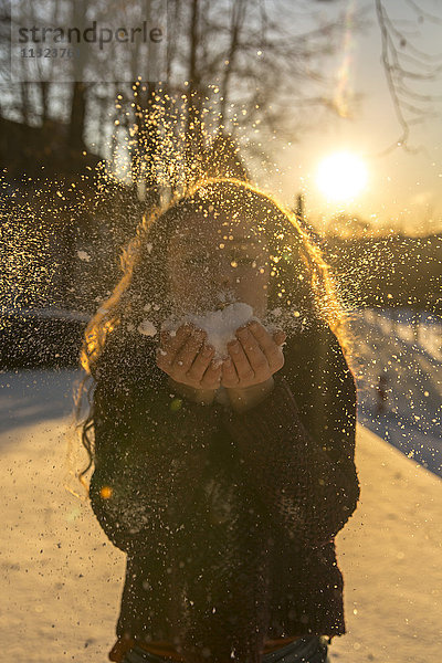 Junge Frau bläst Schnee bei Gegenlicht