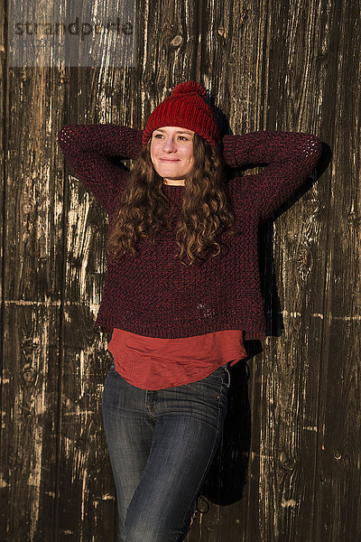 Porträt einer entspannten jungen Frau in Wintermode an der Holzwand lehnend