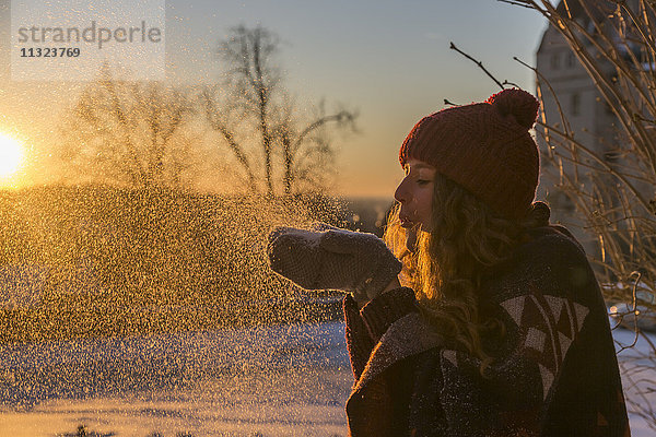 Junge Frau  die bei Sonnenuntergang Schnee bläst