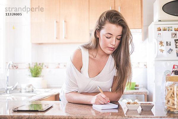Junge Frau schreibt auf Notizblock in der Küche