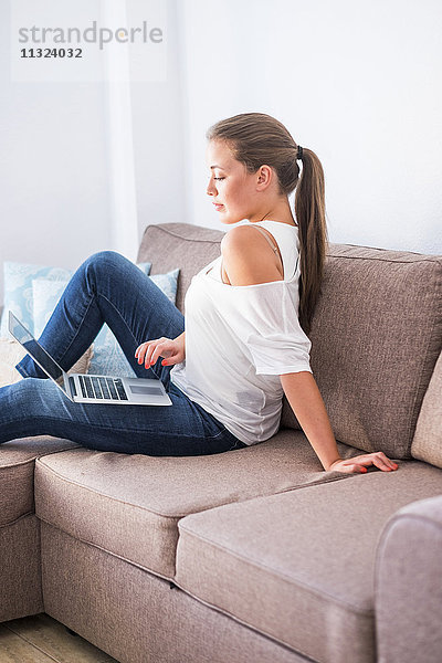 Junge Frau sitzt auf der Couch mit Laptop