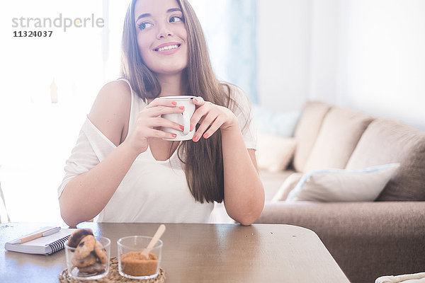 Lächelnde junge Frau trinkt Kaffee zu Hause