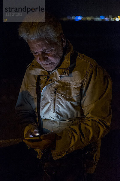Ein älterer Mann  der nachts ein Handy benutzt.