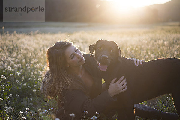 Junge Frau und ihr Hund im Blumenfeld in der Dämmerung