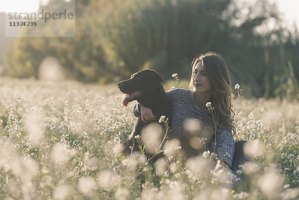 Junge Frau und ihr Hund im Blumenfeld in der Dämmerung