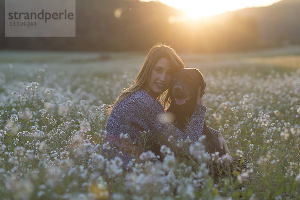 Junge Frau und ihr Hund im Blumenfeld in der Dämmerung