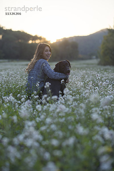 Junge Frau und ihr Hund im Blumenfeld in der Dämmerung