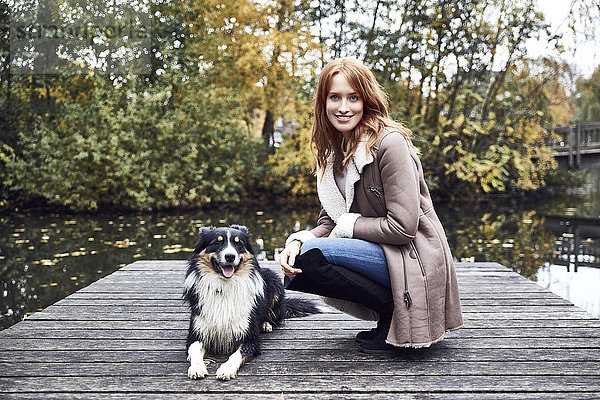 Porträt der lächelnden Frau mit ihrem Hund am Steg im Herbst