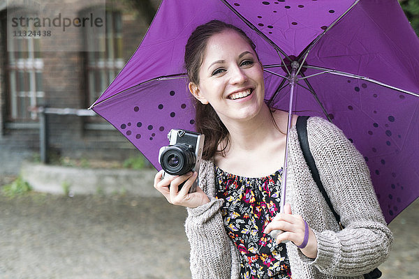Fröhliche junge Frau mit Kamera und Regenschirm Outddors