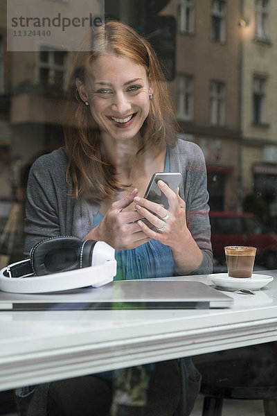 Porträt einer lächelnden Frau mit Smartphone im Café